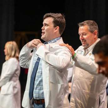 student receives white coat from faculty member