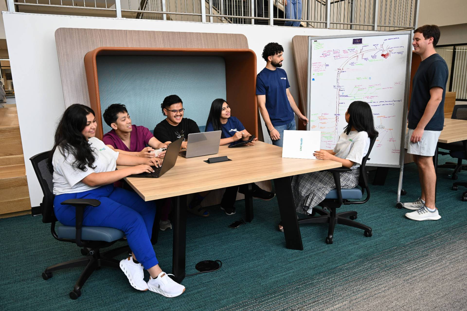 Students work together in the library with laptops and a whiteboard